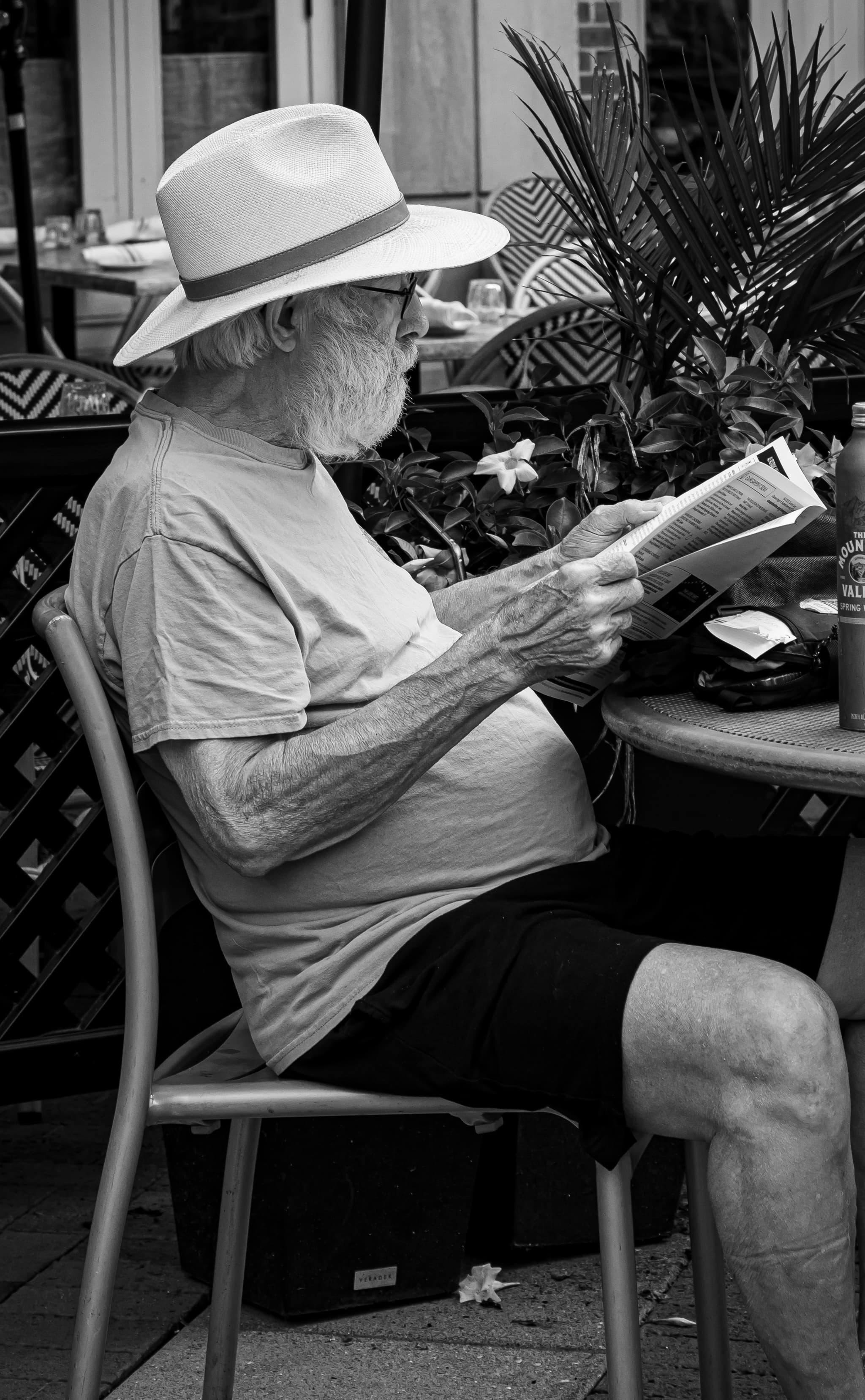 Elderly man in a panama hat reads at an outdoor café